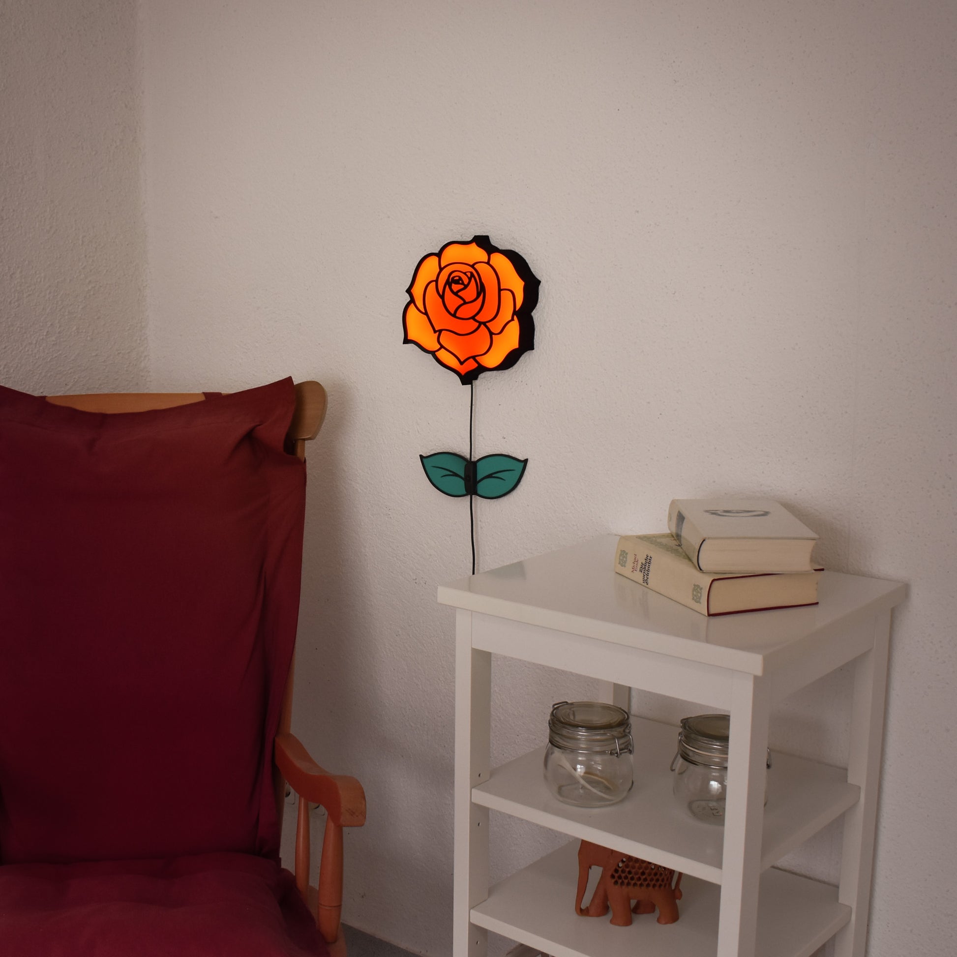 Wandmontierte LED-Rosenlampe leuchtet in warmem Rot über einem weißen Beistelltisch.